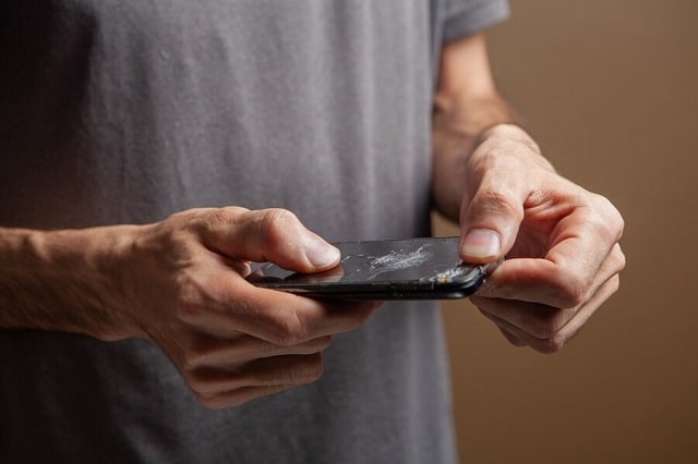 homme tenant un téléphone cassé sur fond marron